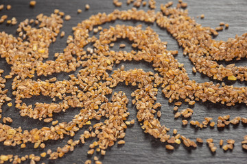 Lot of whole raw bulgur grains waving on grey stone