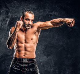 Professional fighter showing kick fighting technique. Studio photo against a dark textured wall