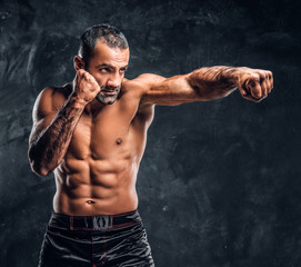 Fototapeta na wymiar Professional fighter showing kick fighting technique. Studio photo against a dark textured wall