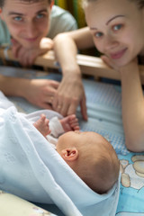 Man and a woman near their newborn. Parents look at the camera. Boy sleeping in his crib. Mom, dad and baby. Portrait of young family. Family life. Man was born.