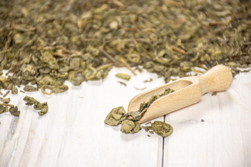 Lot of pieces of dry green tea with wooden scoop on white wood