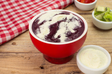 Brazilian acai with baby milk  and fruits in a red bowl in wood background 