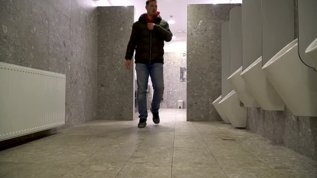 A man going to a public toilet to urinate and then washing his hands
