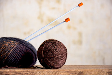 two skeins of wool yarn in brown tones and knitting needles on an old wooden surface close-up, handmade, knitting