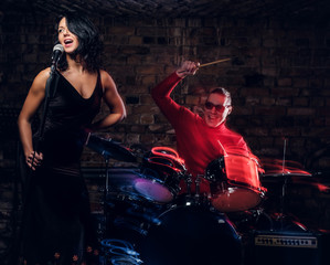 Obraz na płótnie Canvas Jazz band performance. Beautiful singer in elegant dress and drummer in a nightclub