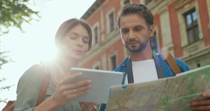 Couple of the Caucasian attractive tourists standing at the street on a summer day and discussing where to go with a map in hands.