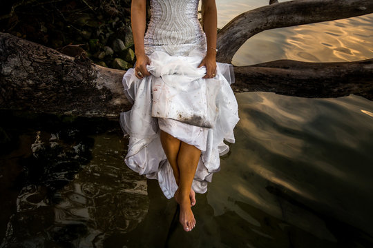 Uma mulher, com seu vestido de noiva, sentada em um galho de &aacute;rvore, por cima da &aacute;gua escura de uma lagoa