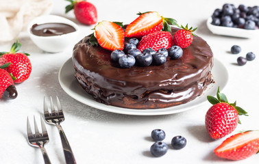 Cheesecake with raisin decorated with chocolate glaze and fresh strawberries and blueberries.