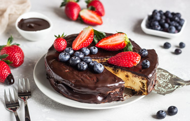 Cheesecake with raisin decorated with chocolate glaze and fresh strawberries and blueberries.