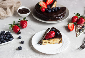 Cheesecake with raisin decorated with chocolate glaze and fresh strawberries and blueberries.
