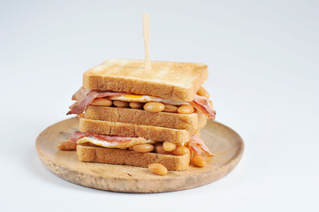 Sandwich with bacon, beans and fried egg on a wooden plate. Light background. Close-up.