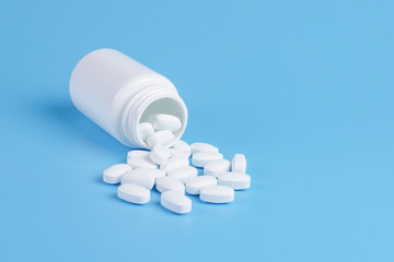 Medicine white pills or tablets drop out of the white bottle on blue background