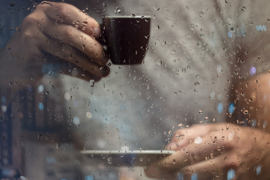 A man stands at the window and drinks coffee. Raindrops on glass.