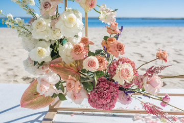 Part of the wedding arch decorated with fresh flowers is set on the sandy bank of the river. Wedding florist arranges workflow