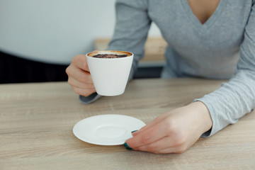 Female in gray sweather hold white cup of coffee