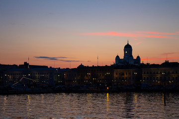 Obraz na płótnie Canvas View of the embankment of Helsinki, houses and the silhouette of the Cathedral of St. Nicholas from the Gulf of Finland at dusk on a bright summer night in the capital of Finland.