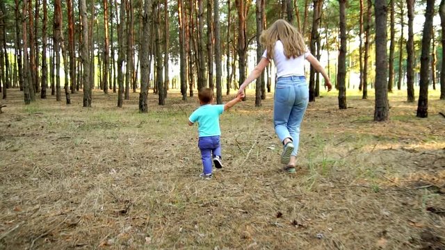 appy family young sister and cute toddler boy running and playing in wild nature pine forest in slow motion