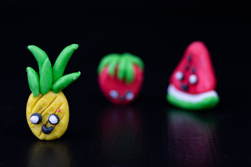 Plasticine figurines on a dark wooden table. Imitation of pineapple, watermelon and strawberry fruit.