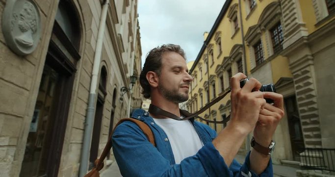 Portrait shot of the handsome Caucasian young man taking photos on the camera on the old town street.