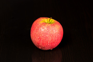 Red ripe Apple in drops of water lying on the table on a black background