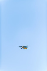 An-2 aircraft in the sky. Blue sky. Agricultural aircraft. Sunny day. Tree with green leaves. Yellow plane with blue wings.