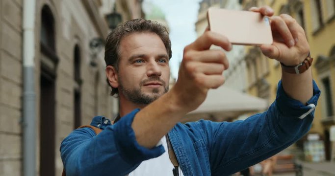 Young handsome Caucasian man taking photos on the smartphone camera as a tourist on the street.