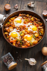 Homemade Hearty Breakfast Skillet with Eggs Potatoes and minced meat on wooden table.