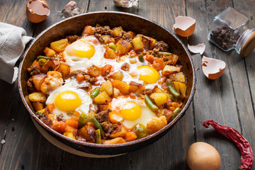 Homemade Hearty Breakfast Skillet with Eggs Potatoes and minced meat on wooden table