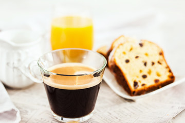 Continental breakfast table with cup of hot black coffee, milk, cakes and orange juice