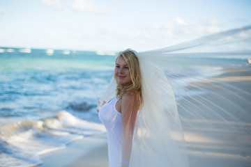 Fototapeta na wymiar Young sexy blonde woman in white dress and bridal veil near sea. Girl at the beach
