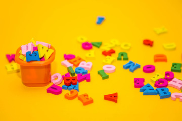 Fototapeta na wymiar Many multicolored wooden letters on a yellow background. toy letters. letters in an orange bucket. english alphabet. design concept. View from above. Flat lay. Copy space for text.
