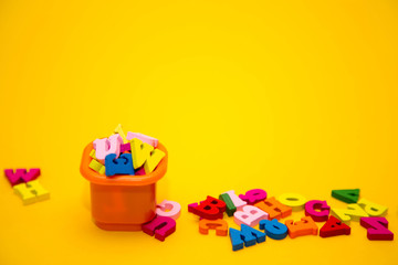  Many multicolored wooden letters on a yellow background. toy letters. letters in an orange bucket. english alphabet. design concept. View from above. Flat lay. Copy space for text.