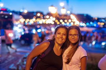 Mother and daughter look at camera together, blurred background at night,