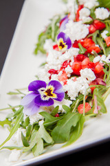 Salad made of cottage cheese, rocket salad, strawberries, pomegranates, onion decorated with flowers