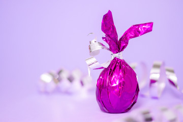 Obraz na płótnie Canvas Easter greeting card with candies colored purple egg bunny ears on violet serpentine background. Minimal style, trendy purple colors.