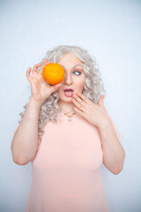 charming plump curly blonde in pink dress with orange on white solid studio background alone