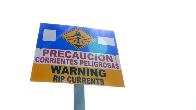 Sign in Spanish and English warning of rip currents. Precaucion corrientes peligrosas. Surfing beach on Pacific Ocean, Guanacaste Province, Costa Rica, Central America. 
