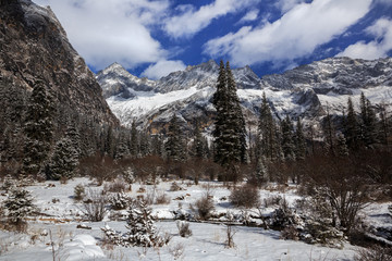 Siguniangshan - Four Girls Mountain National Park in Sichuan Province, China. ShuangQiao Valley Scenic Area, Snow Capped Jagged Mountains with clouds forming at the summit. Blue Sky, Snow Mountains