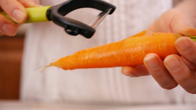 Woman hands hold and peel fresh carrot with green leaves - close up, slow motion, camera slide
