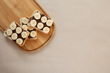 Three banana white bread toasts smeared with chocolate butter that lie on a cutting board on craft paper background. top view with area for text