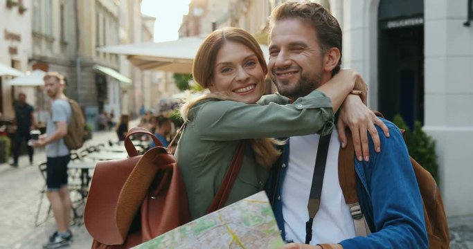 Portrait of the attractive smiled romantic couple looking at the map and deciding where to go, choosing a route while standing on the street of city.
