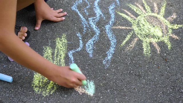 Closeup top view of child's little hand holding piece of blue chalk and drawing sea water on pavement of sidewalk outdoors at city park. Child drawing tropical beach. Real time 4k video footage.