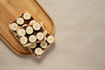 Three banana white bread toasts smeared with chocolate butter that lie on a cutting board on craft paper background. top view with area for text