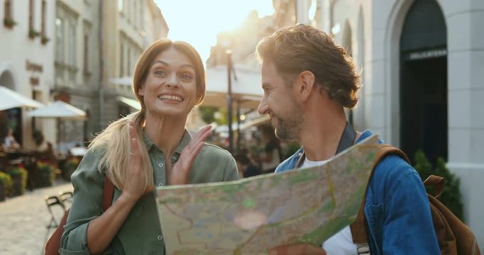 Portrait of the Caucasian cheerful romantic couple lost in the city while sightseeing and reading a map, then finding the way.