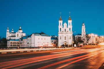 Fototapeta na wymiar Vitebsk, Belarus. Traffic At Street And Holy Assumption Cathedral, Holy Resurrection Church And City Hall In Evening Or Night Illumination At Winter
