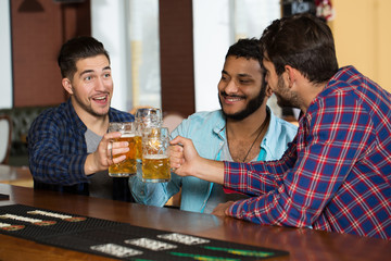 Cheers! Male friends having beer at the pub cheering with their drinks laughing