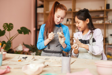 Portrait of two girls shaping clay while making handmade ceramics in pottery class, copy space