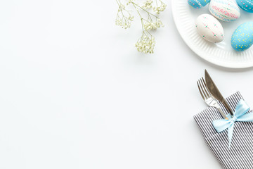 Easter table decoration in blue colors. Plate, cutlery, painted eggs and dry flower branch, tablecloth on white background top view