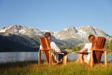Couple in Adirondack chairs by June Lake with Sierra Nevada Mountains in distance - obrazy, fototapety, plakaty