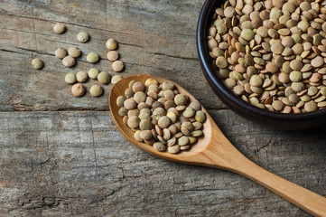 Green lentils in wooden spoon or shovel on wooden background. Uncooked green lentil legumes, herbaceous plant (Lens culinaris)